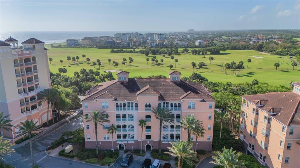 An aerial view shows three multi-story peach-colored apartment buildings overlooking a green golf course — 5 OCEAN CREST WAY UNIT 1411, PALM COAST, FL