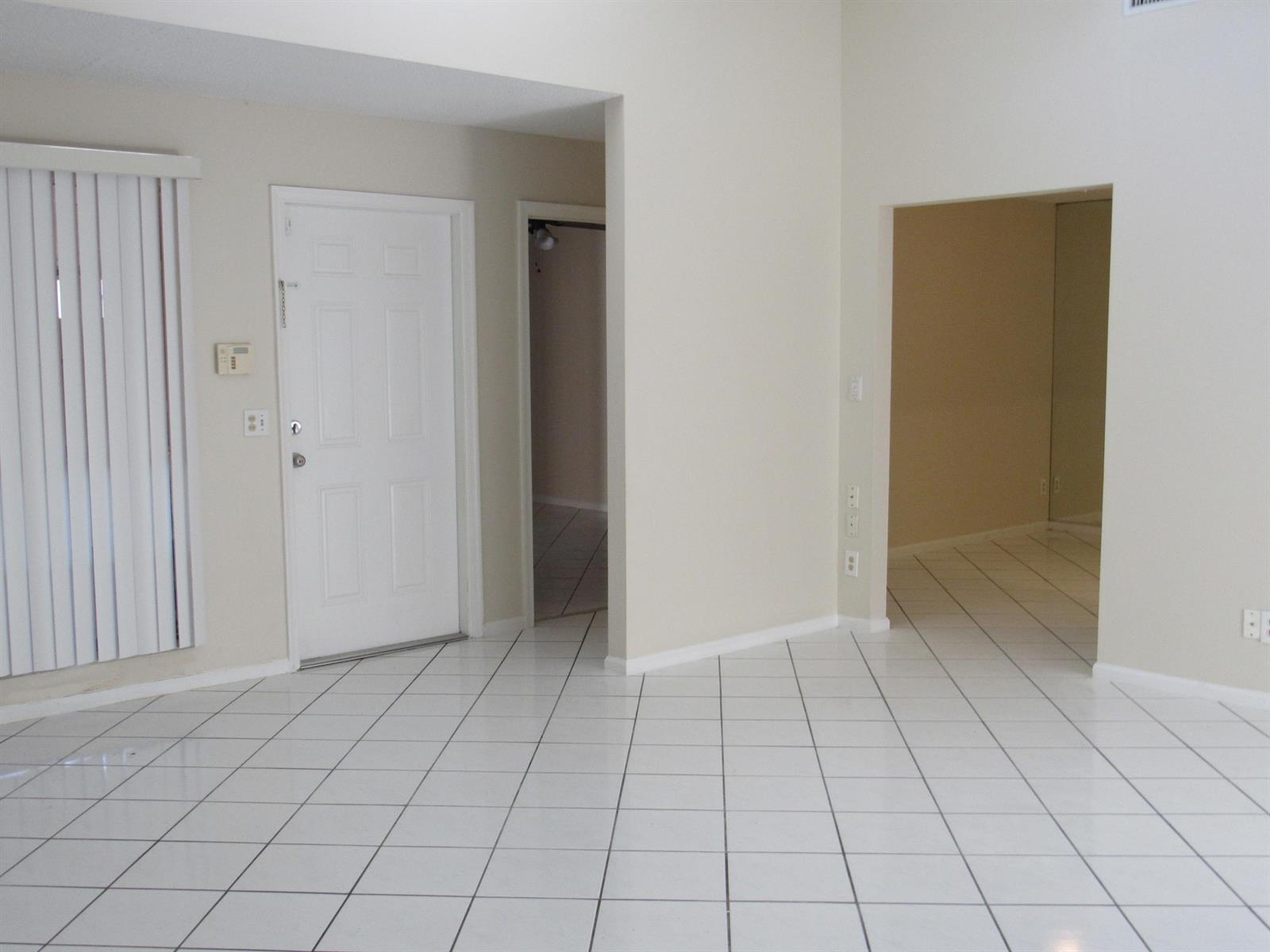A bright entryway with white tiled floors, a white front door, and two arched doorways — 1065 Manor Drive, Palm Springs FL 33461, PALM SPRINGS, FL