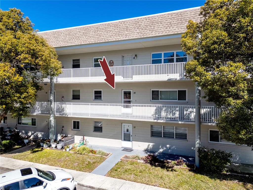 A three-story apartment building exterior with a red arrow pointing to a second-floor unit — 2440 WORLD PARKWAY BOULEVARD UNIT 38, CLEARWATER, FL