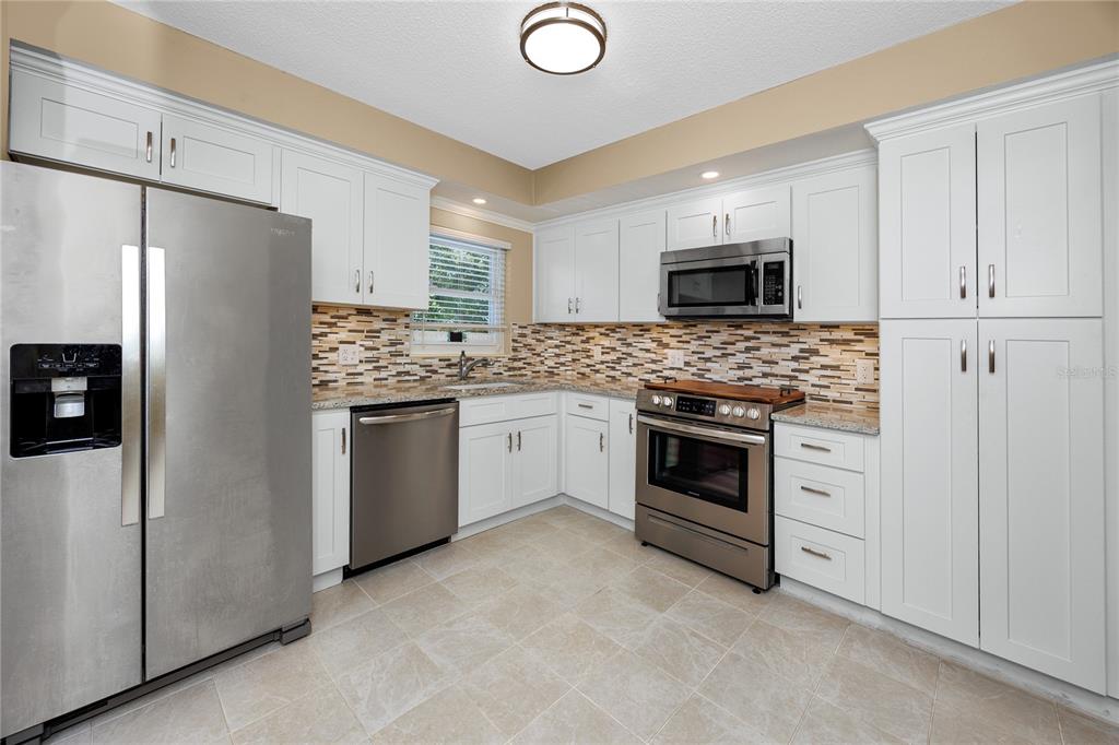 A stainless steel microwave and oven range are set against a tiled backsplash and cabinets — 2440 WORLD PARKWAY BOULEVARD UNIT 38, CLEARWATER, FL