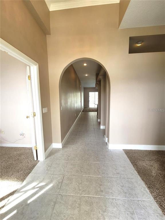 A tiled hallway with an arched entryway leads toward a doorway in the distance — 1501 DEERBOURNE DRIVE, WESLEY CHAPEL, FL