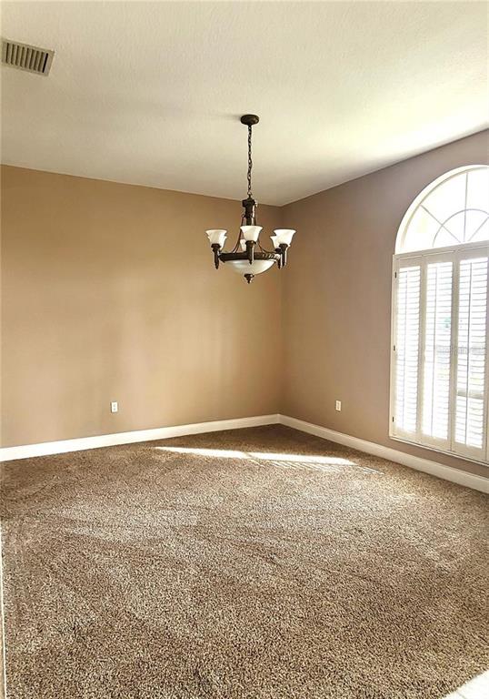 An empty dining room features beige walls, brown carpeting, and a traditional chandelier — 1501 DEERBOURNE DRIVE, WESLEY CHAPEL, FL