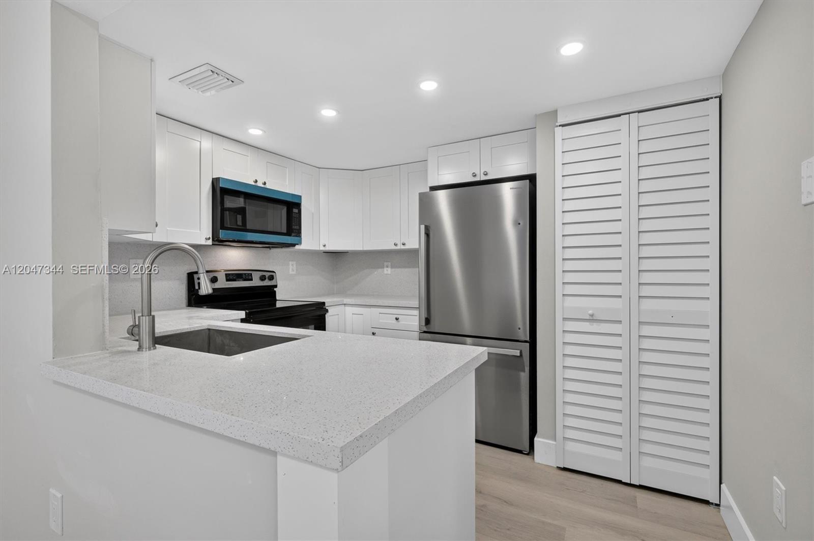 A kitchen features white cabinetry, stainless steel appliances, and light-colored quartz countertops — 10080 NW 9th St Cir # 204, Miami FL 33172, MIAMI, FL