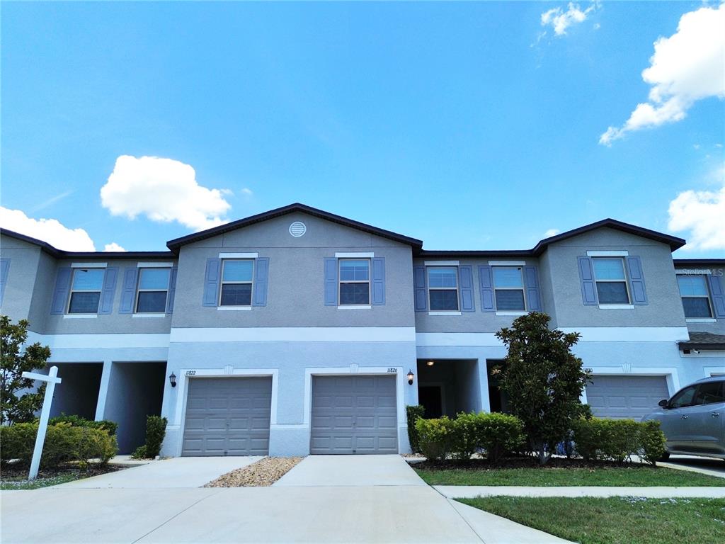 A two-story townhouse exterior features gray stucco walls, blue shutters, and two attached garages — 11826 DUMAINE VALLEY ROAD, RIVERVIEW, FL