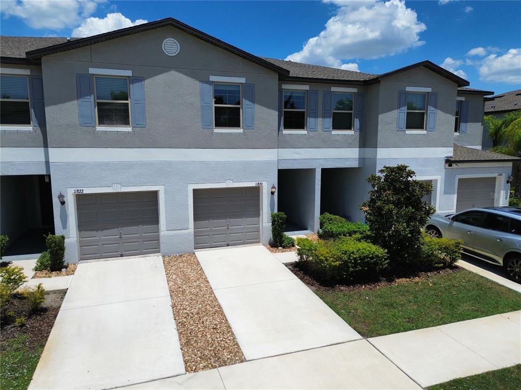 An exterior view of a two-story townhouse complex with gray stucco walls and attached garages — 11826 DUMAINE VALLEY ROAD, RIVERVIEW, FL
