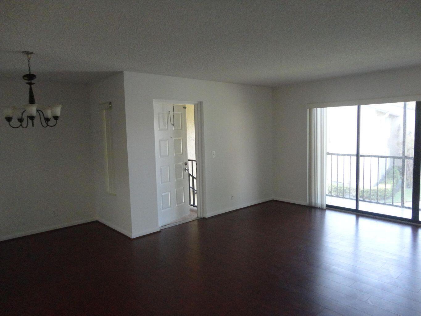 An empty room features dark wood-look flooring, a white front door, and a sliding glass door — 714 Sunny Pine Way # C2, FL 33415, FL