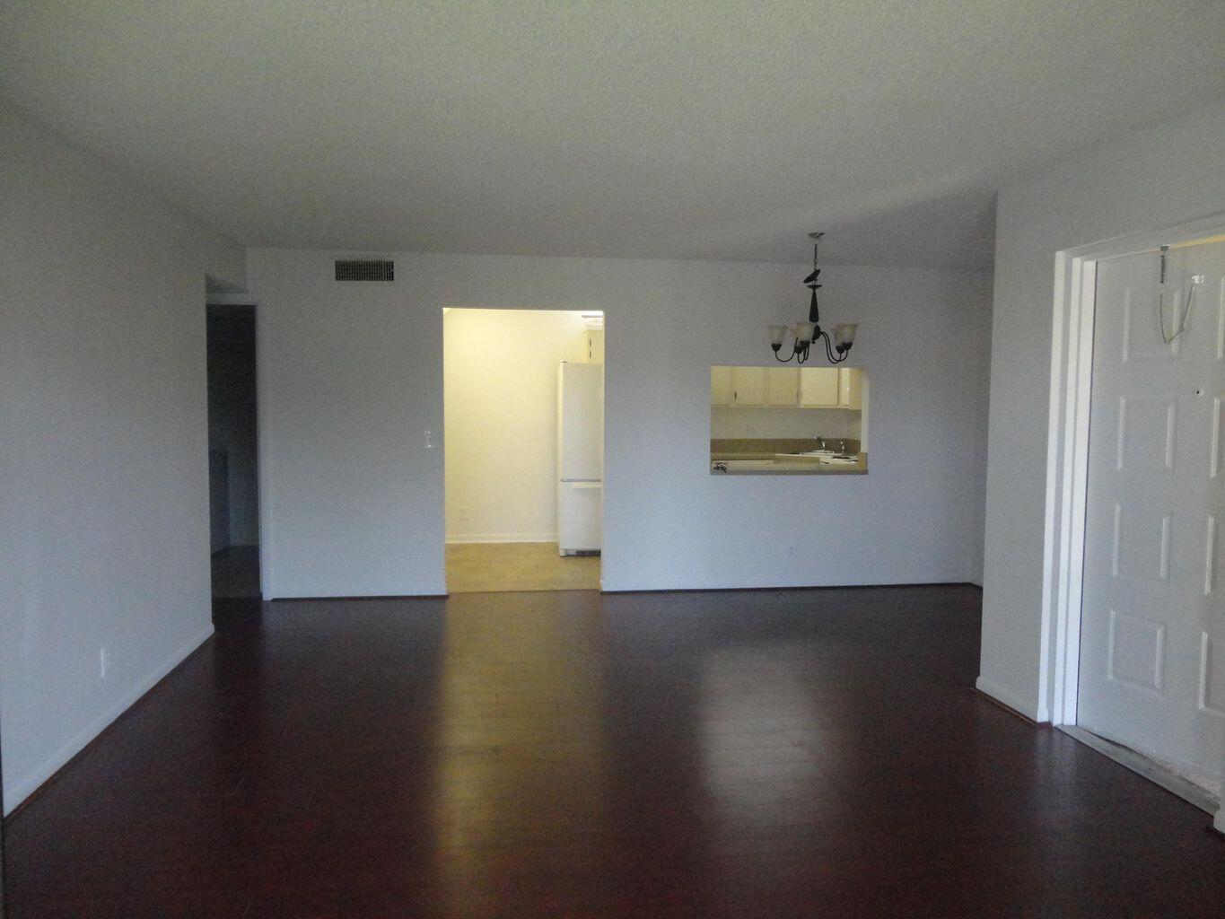An empty living room with dark wood-look flooring, a kitchen pass-through, and a chandelier — 714 Sunny Pine Way # C2, FL 33415, FL