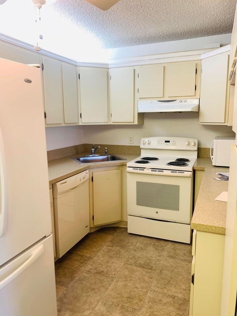 A kitchen with white appliances, beige cabinets, laminate countertops, and light-colored tile flooring — 714 Sunny Pine Way # C2, FL 33415, FL