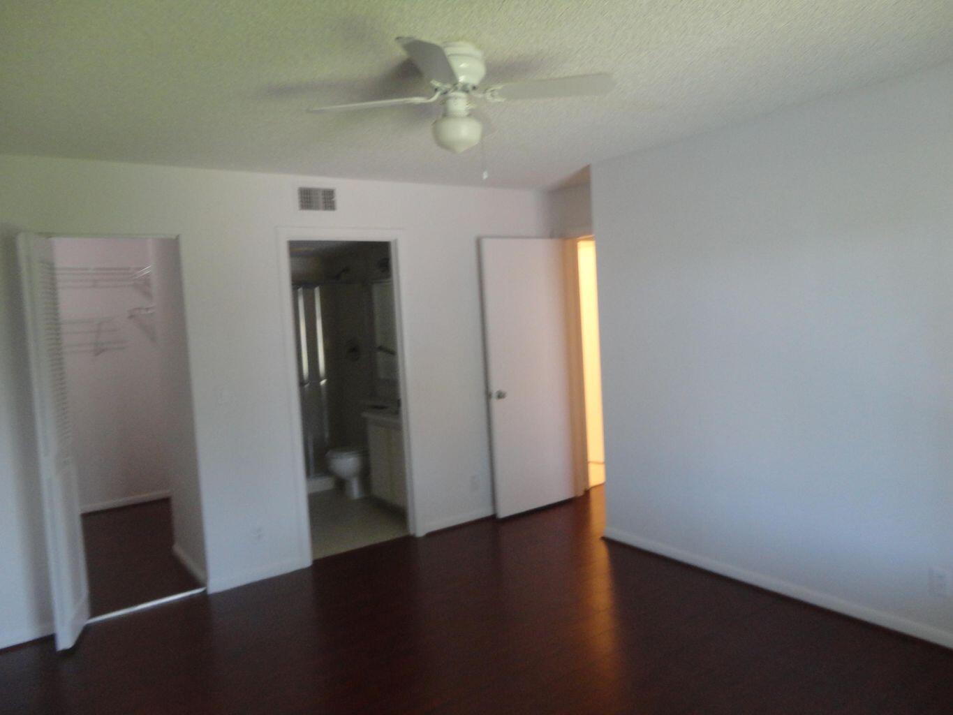 An empty bedroom features dark wood flooring, white walls, a ceiling fan, and closet access — 714 Sunny Pine Way # C2, FL 33415, FL