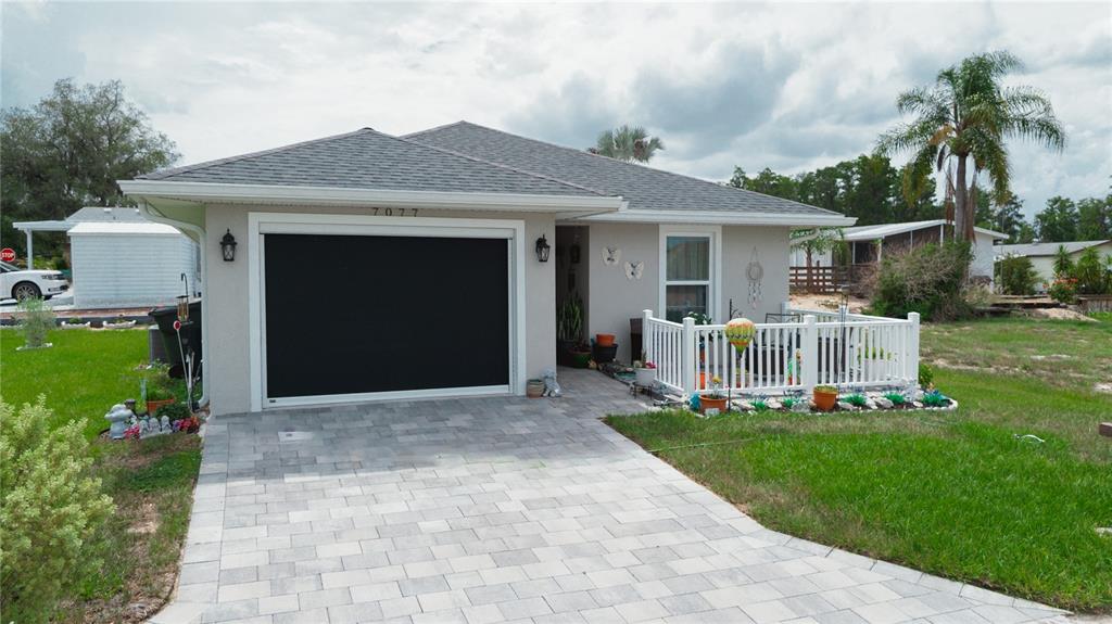 A single-story house features a paved driveway, a black garage screen, and a white-fenced porch — 7077 TAMARIND WAY, LAKE WALES, FL