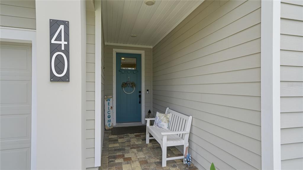 A covered entryway features a blue front door, a white bench, and a house number sign — 40 MOANA COURT S, PALM COAST, FL