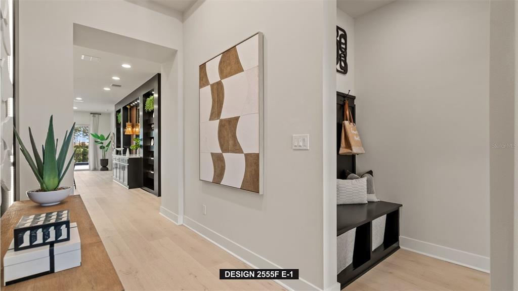 A hallway features light wood flooring, a geometric wall painting, and a black mudroom bench — 9535 SANDY SHORES STREET, PARRISH, FL
