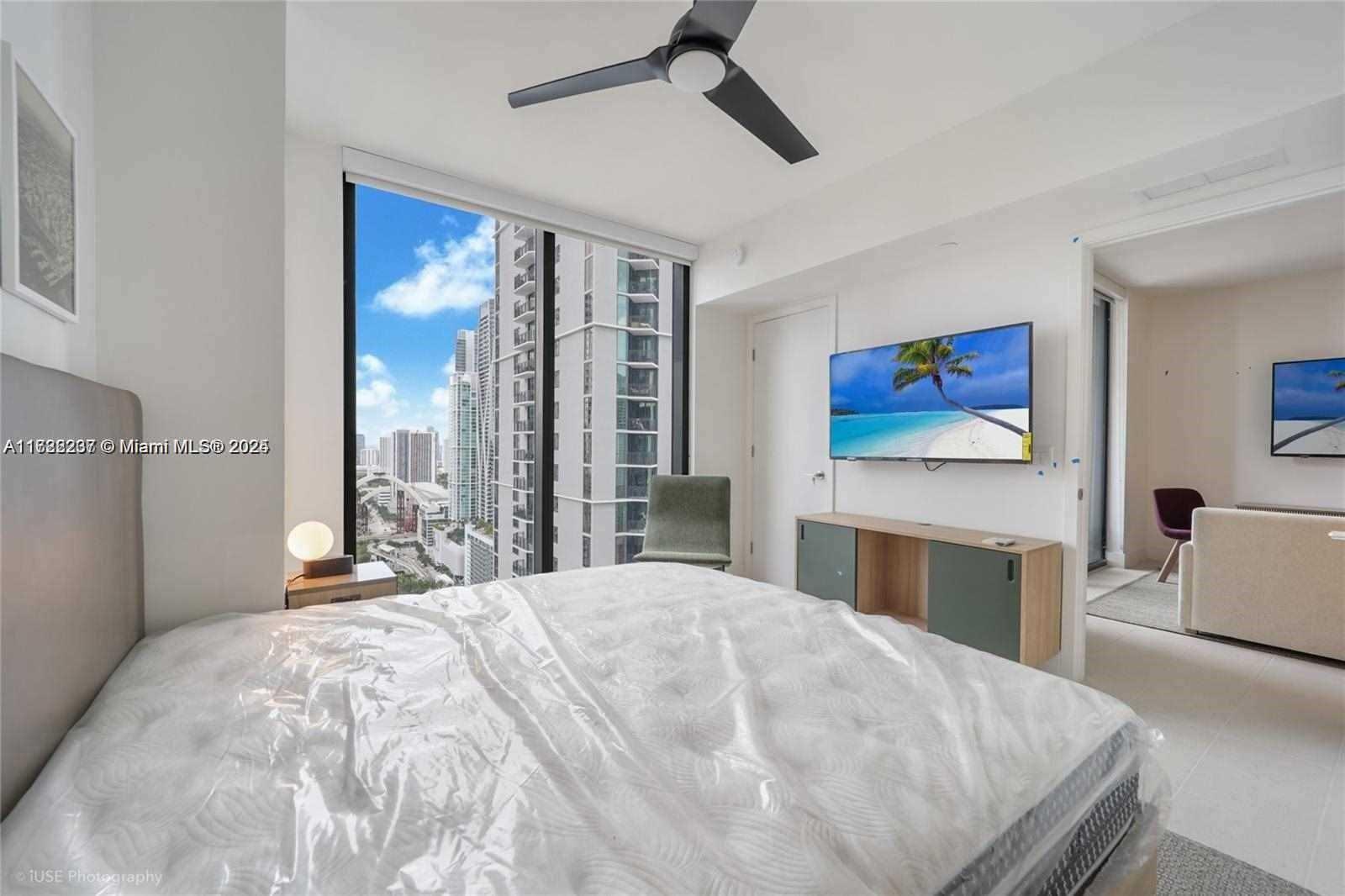 A bedroom features a bed with a plastic-covered mattress, a wall-mounted television, and floor-to-ceiling windows — 159 NE 6 # 3913, Miami FL 33132, MIAMI, FL