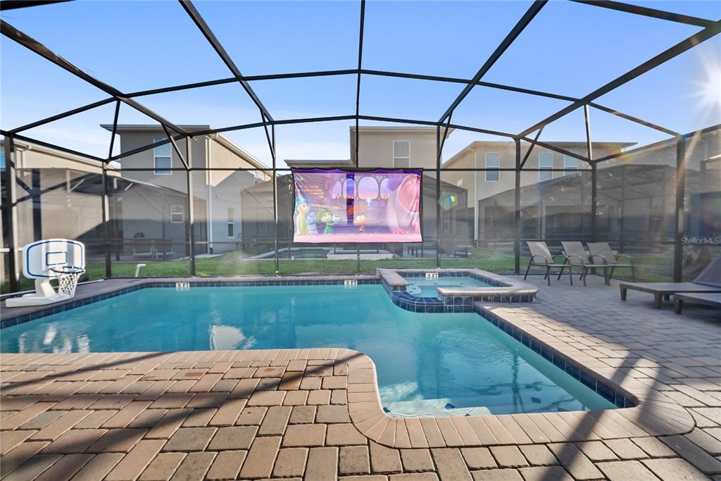 A screened-in swimming pool and hot tub area with a projector screen and patio furniture — 4526 NARRATIVE LANE, KISSIMMEE, FL