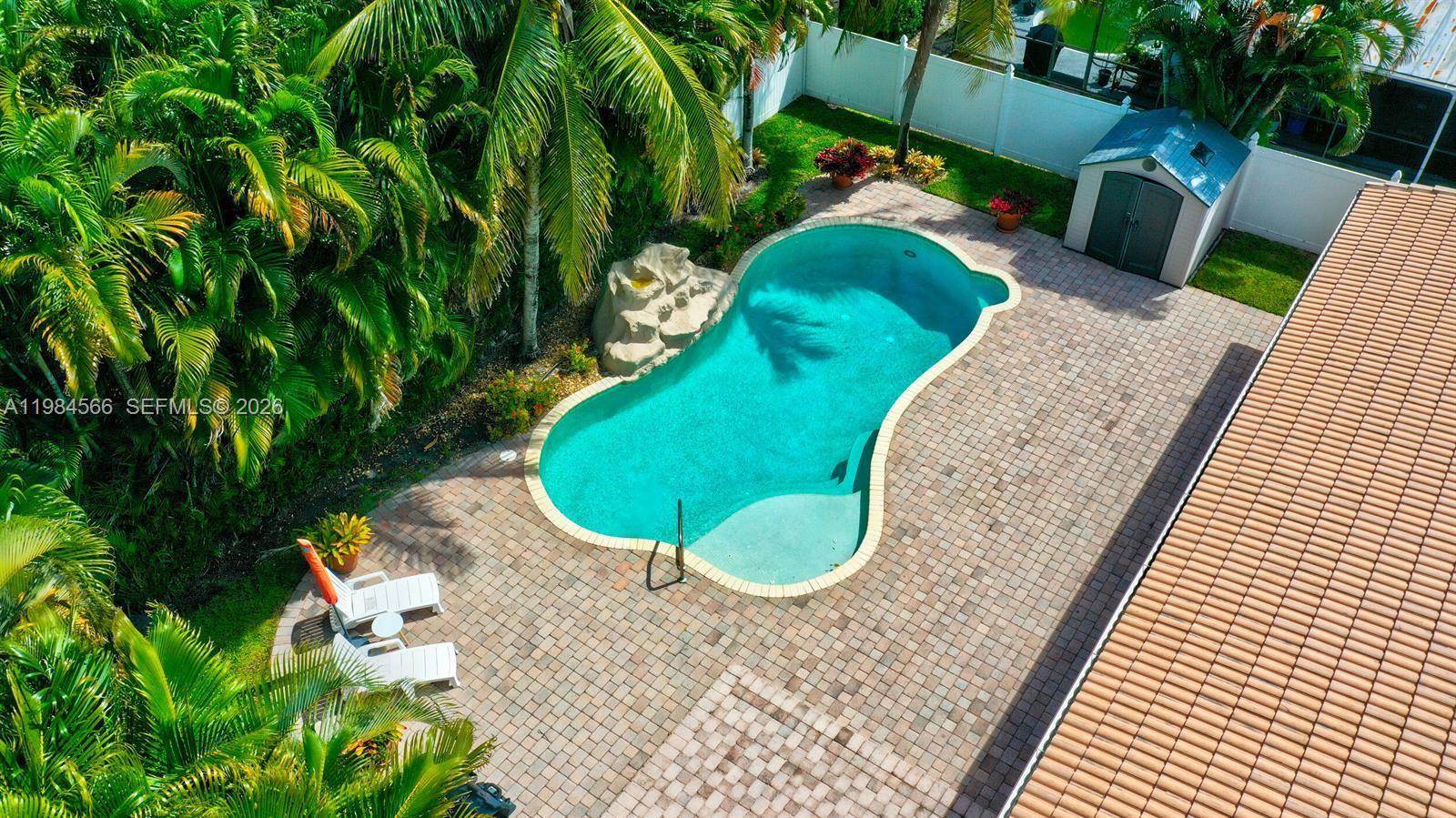 An aerial view shows a backyard with a kidney-shaped pool, rock feature, and patio — 11 Forest Hills Ln, Boca Raton FL 33431, BOCA RATON, FL