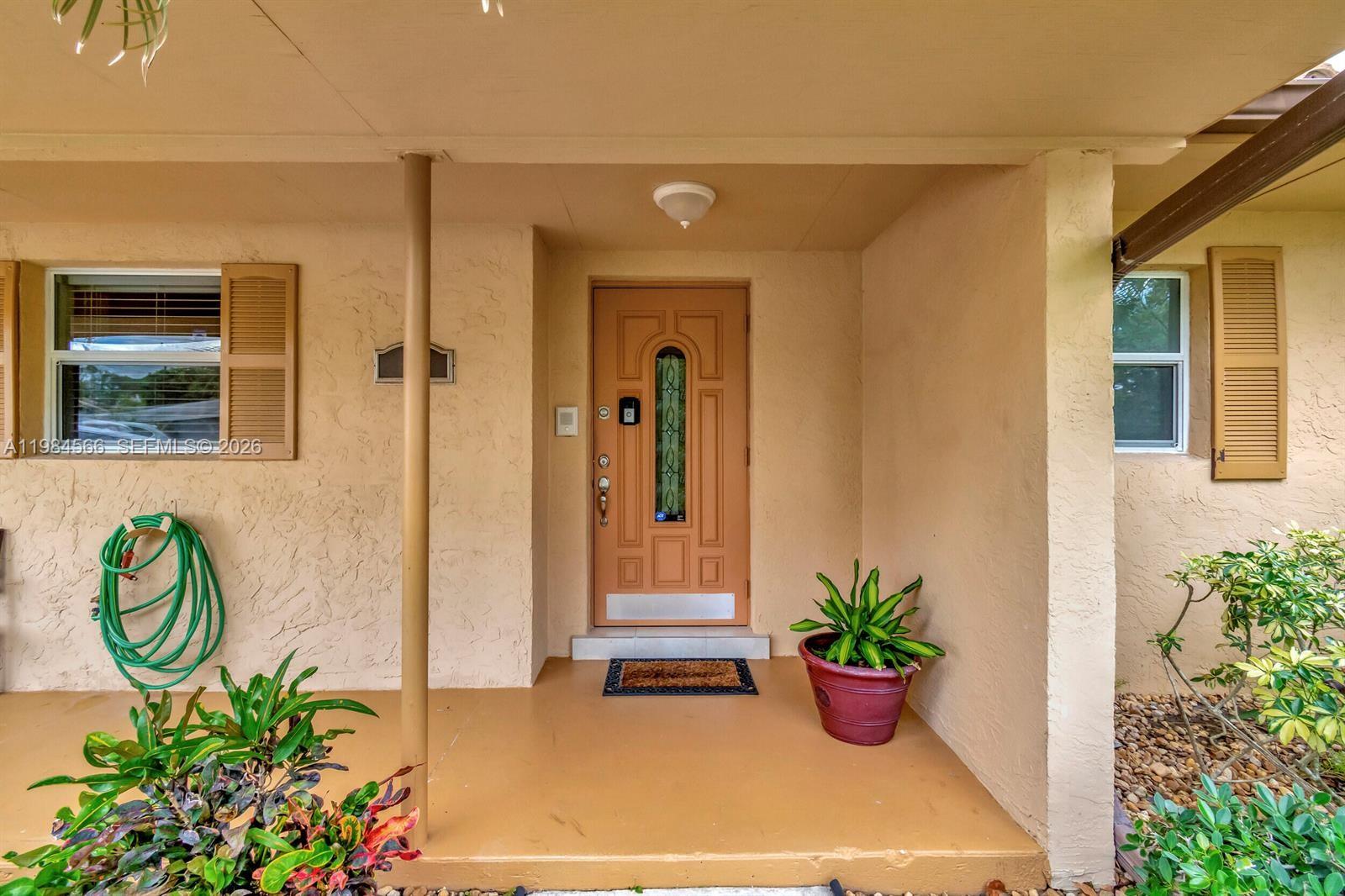 A covered front porch features a tan door, a potted plant, and a green hose — 11 Forest Hills Ln, Boca Raton FL 33431, BOCA RATON, FL