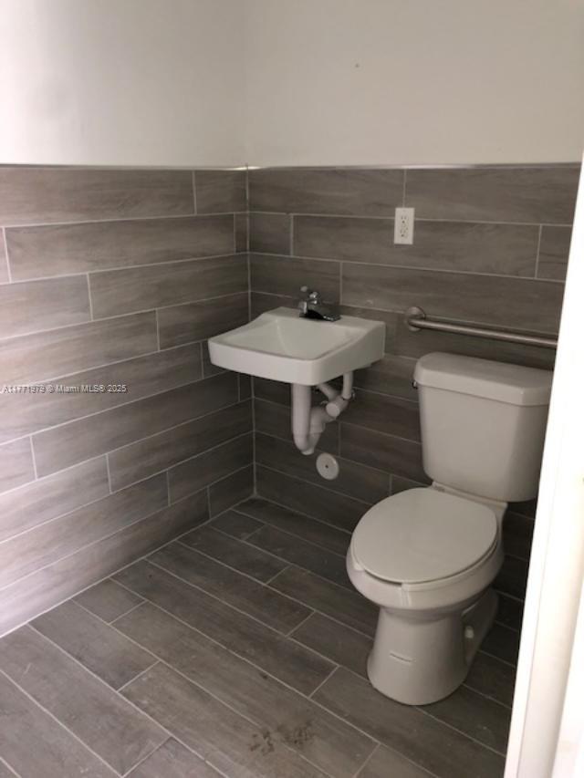 A small bathroom features a wall-mounted sink, a white toilet, and gray wood-look tile — 2201 NW 27th Ave # 2201, Miami FL 33142, MIAMI, FL
