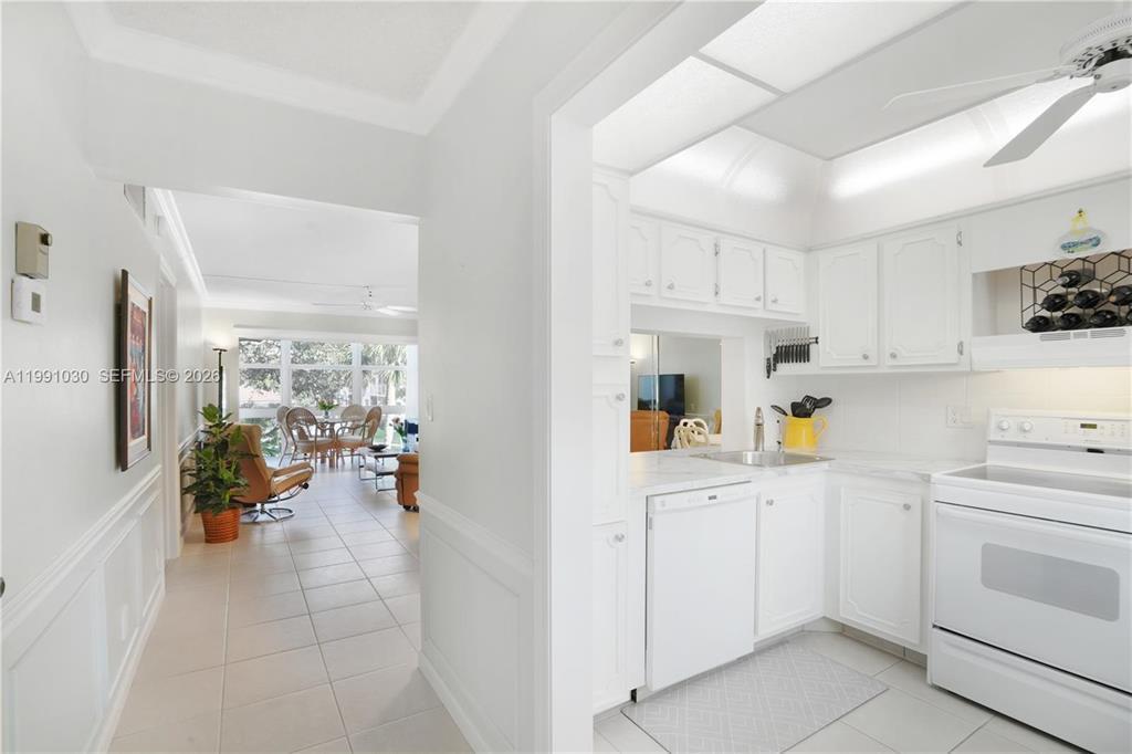 A white kitchen with a pass-through window overlooks a bright living area with tile floors — 1501 S Ocean Boulevard # 214, Pompano Beach FL 33062, POMPANO BEACH, FL