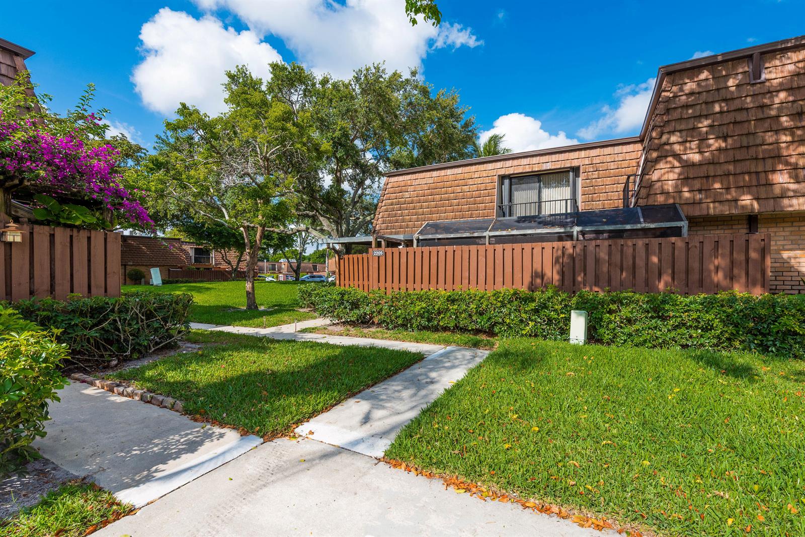 A brown townhouse exterior with a wooden fence, a small lawn, and a concrete walkway — 2205 22nd Lane, FL 33463, FL