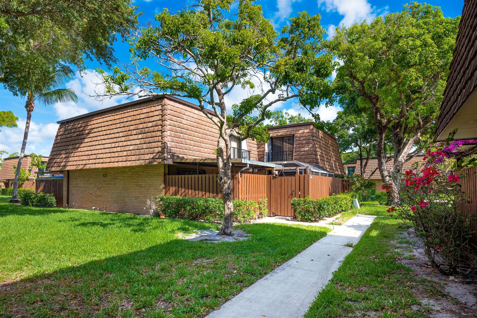 A two-story townhouse with a brown mansard roof, brick exterior, and a wooden privacy fence — 2205 22nd Lane, FL 33463, FL