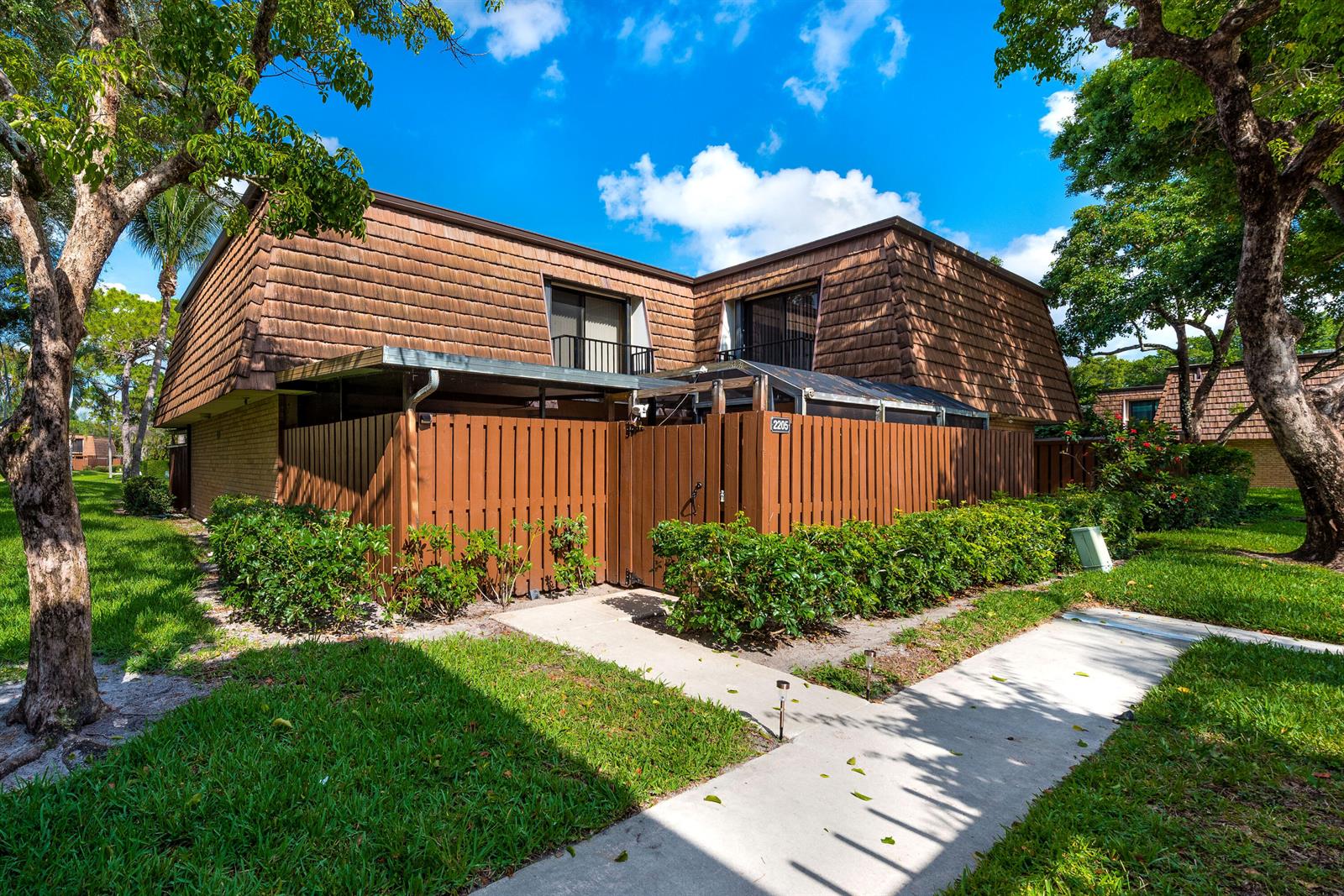 A two-story townhouse exterior with a brown shingled mansard roof and a private fenced courtyard — 2205 22nd Lane, FL 33463, FL