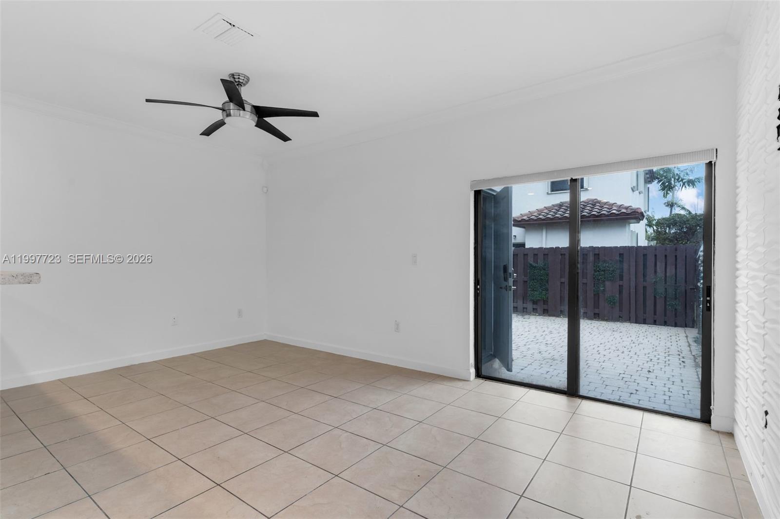 An empty room with white walls, tile flooring, a ceiling fan, and sliding glass doors — 3202 SE 6th St, Homestead FL 33033, HOMESTEAD, FL