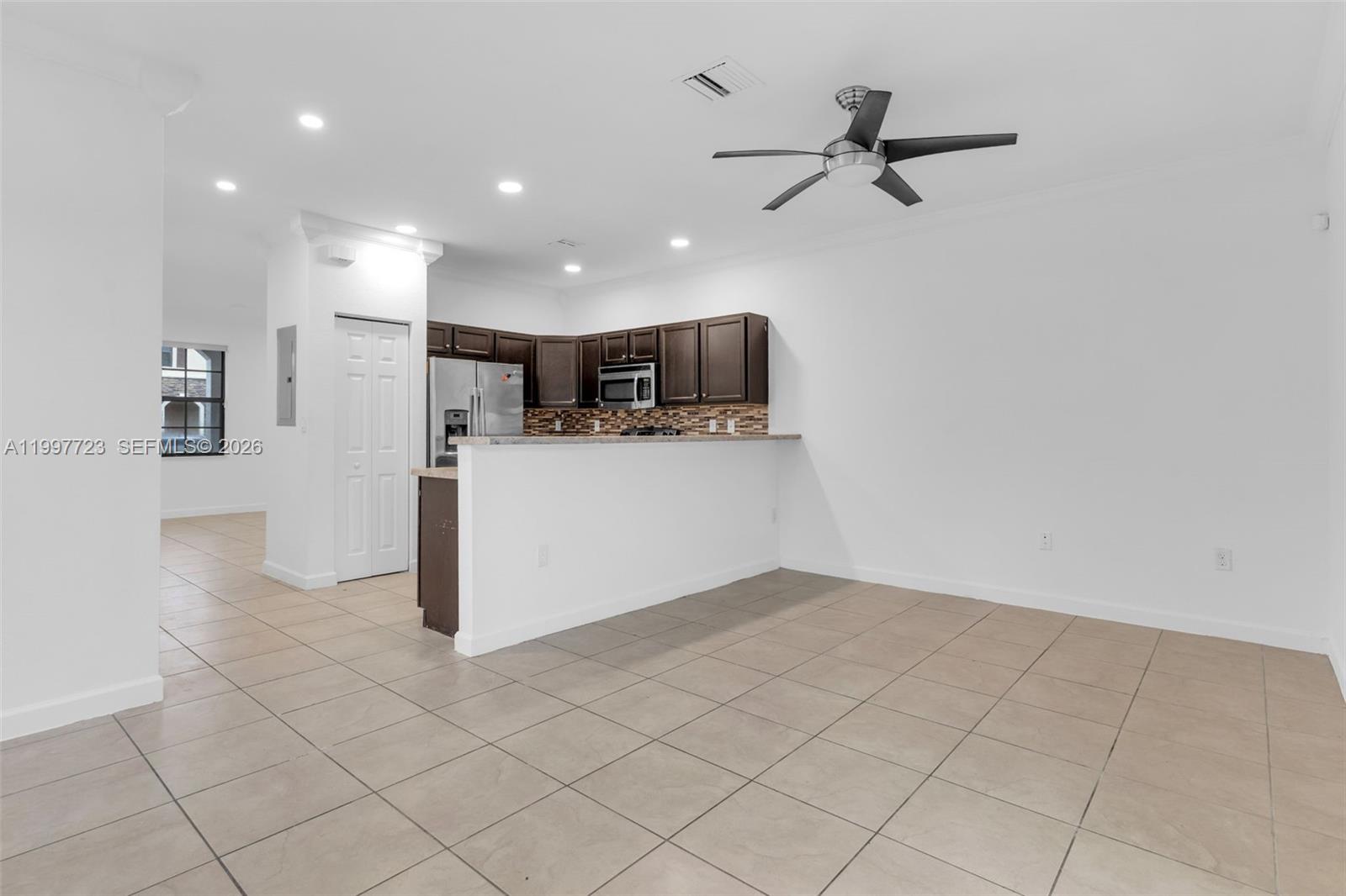 An open-concept kitchen with dark wood cabinets and a breakfast bar overlooks a tiled room — 3202 SE 6th St, Homestead FL 33033, HOMESTEAD, FL