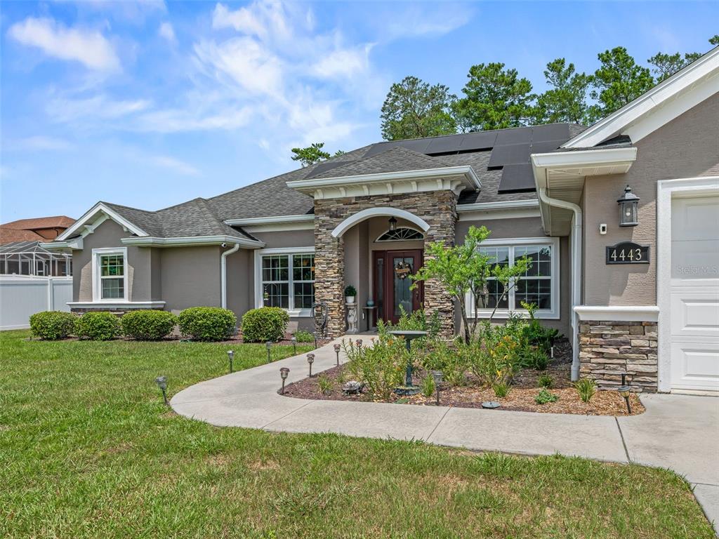 A single-story house with a stone-accented entryway, solar panels, and a concrete walkway — 4443 SW 108TH PLACE, OCALA, FL