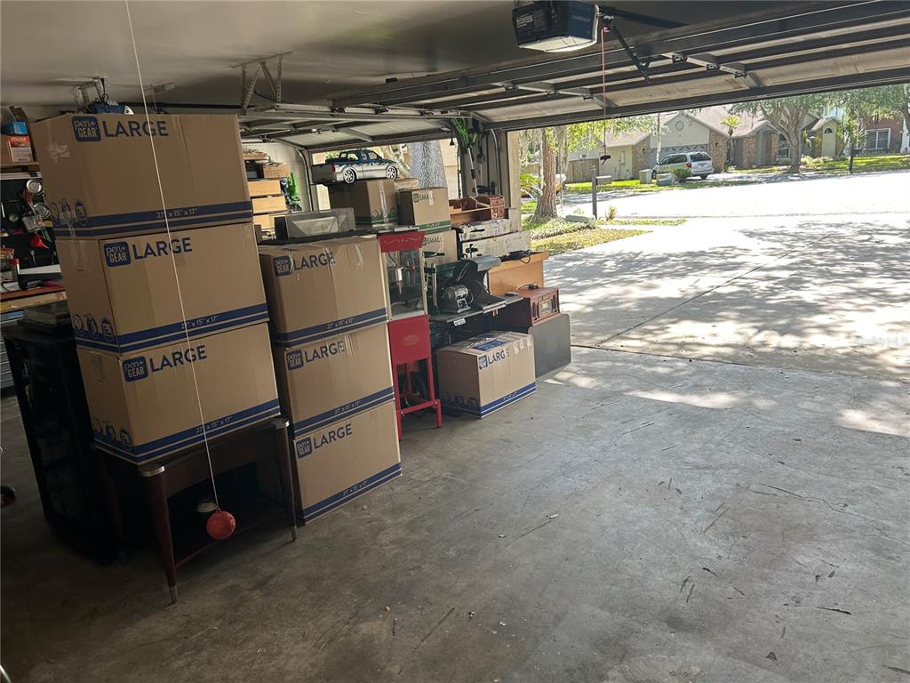 A garage contains several stacked cardboard moving boxes and various household items — 1729 BUCKHORN PLACE, ORLANDO, FL