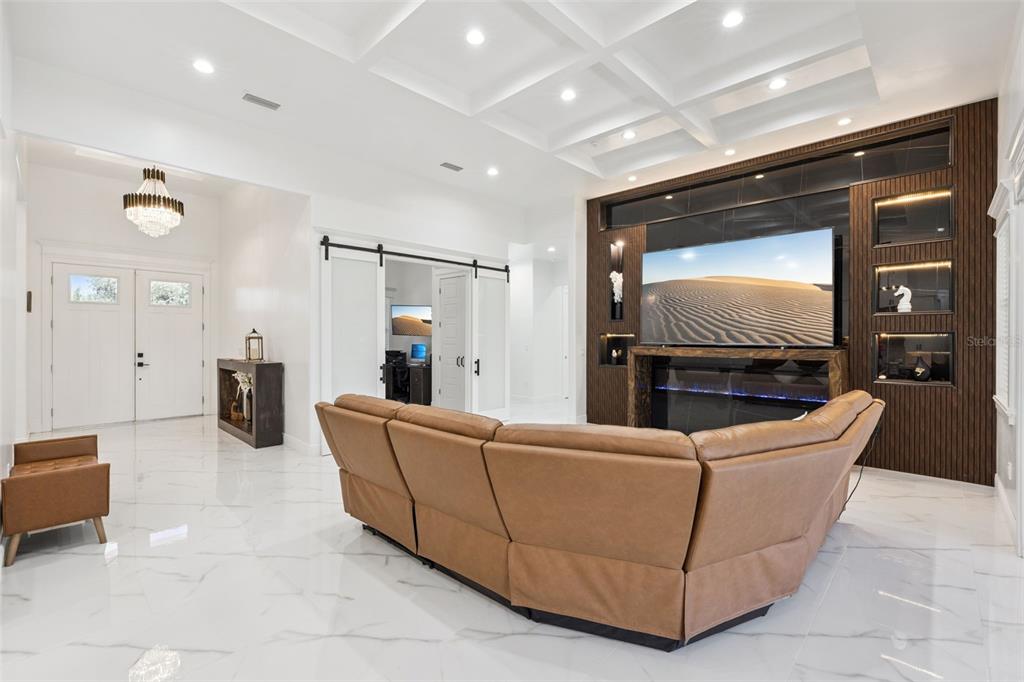 A modern living room features a coffered ceiling, marble floors, and a large media wall — 7739 N CHERRY LAKE GROVES ROAD, GROVELAND, FL