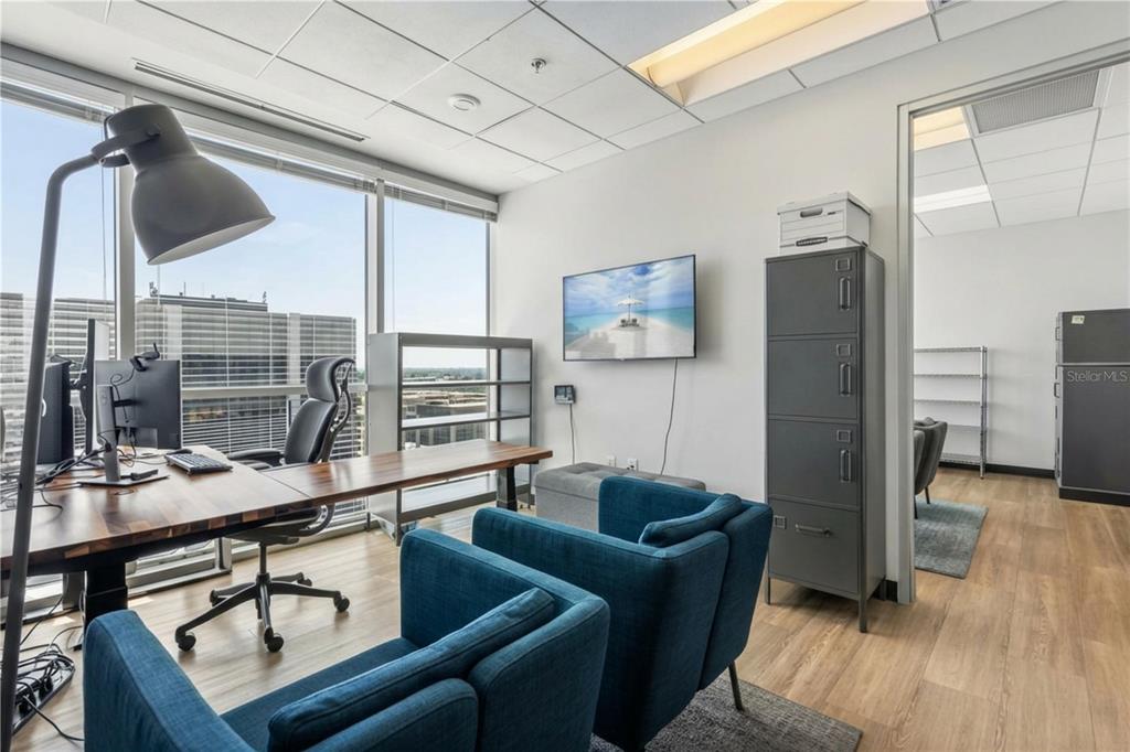 A modern office features a wooden desk, two blue armchairs, a wall-mounted television, and windows — 189 S ORANGE AVENUE UNIT 1950S, ORLANDO, FL