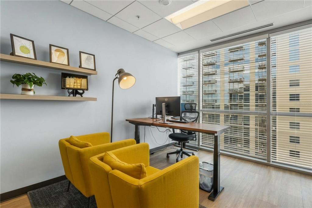A home office features two yellow armchairs, a standing desk, floating shelves, and floor-to-ceiling windows — 189 S ORANGE AVENUE UNIT 1950S, ORLANDO, FL