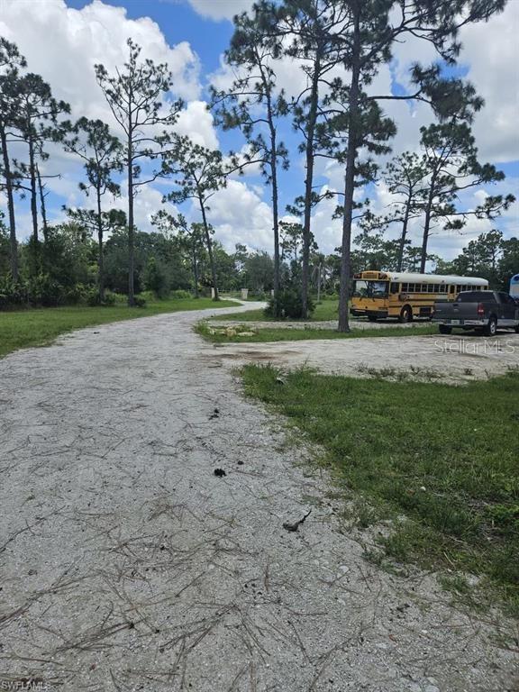 A gravel driveway leads toward a school bus and a pickup truck parked among trees — 1375 W ASH ROAD, LABELLE, FL