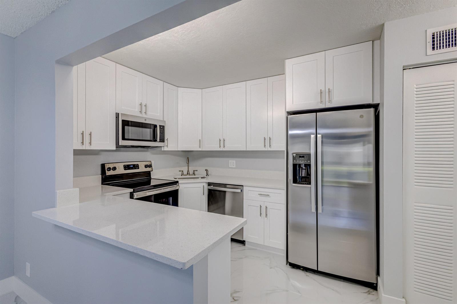 A modern kitchen features white cabinets, stainless steel appliances, and white quartz countertops — 4821 Sable Pine Circle, West Palm Beach FL 33417, WEST PALM BEACH, FL