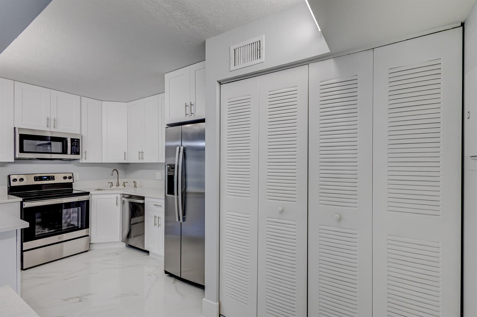 A modern kitchen features white cabinetry, stainless steel appliances, and white marble-patterned tile flooring — 4821 Sable Pine Circle, West Palm Beach FL 33417, WEST PALM BEACH, FL
