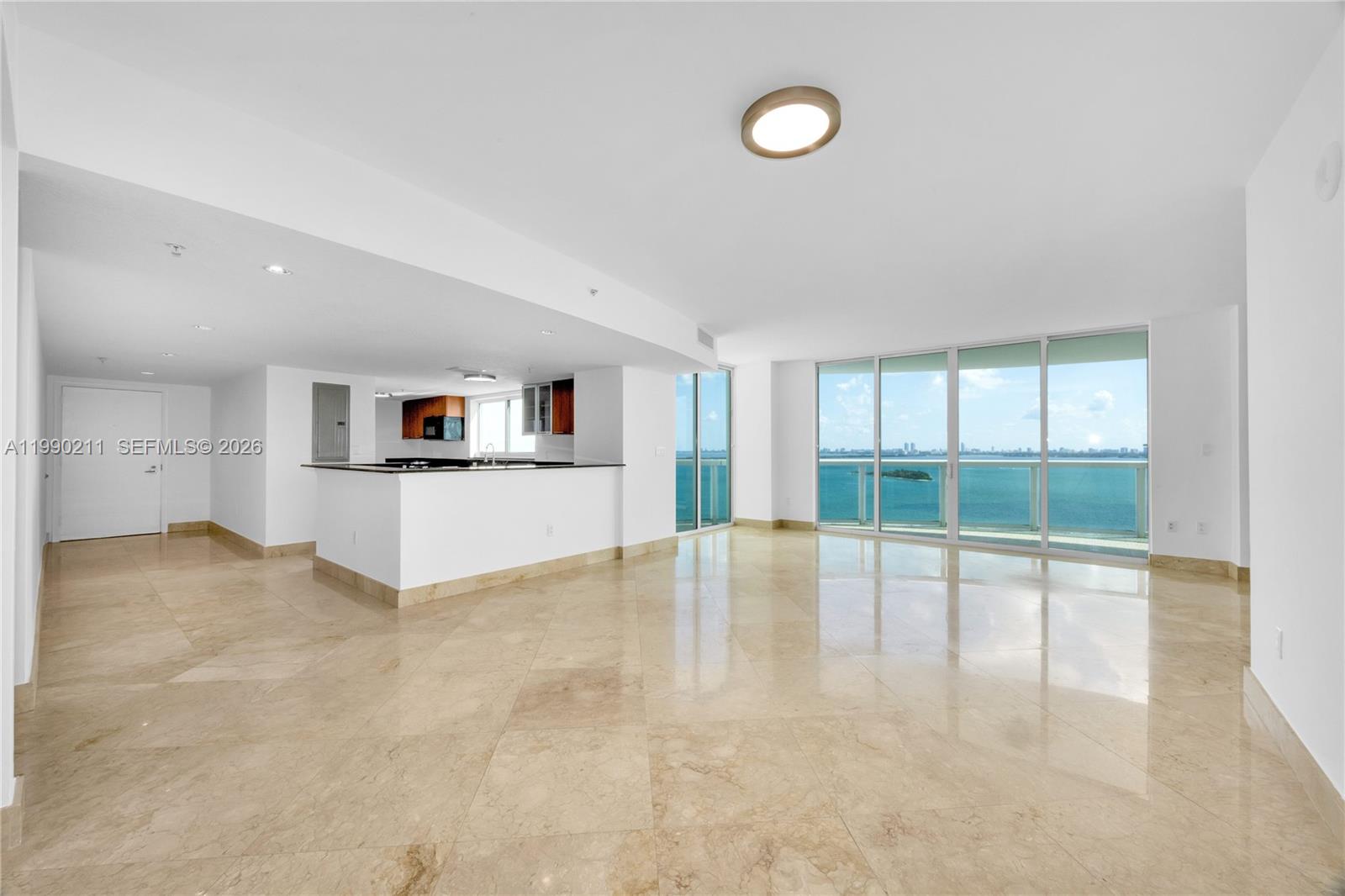 An open-concept living area features beige marble floors, white walls, and floor-to-ceiling windows overlooking water — 1800 N Bayshore Dr # 1901, Miami FL 33132, MIAMI, FL