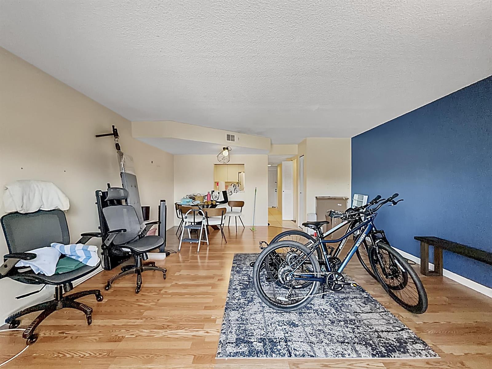 A living area with hardwood floors, a blue accent wall, and two bicycles on a rug — 65 Deer Creek Road # H206, Deerfield Beach FL 33442, DEERFIELD BEACH, FL