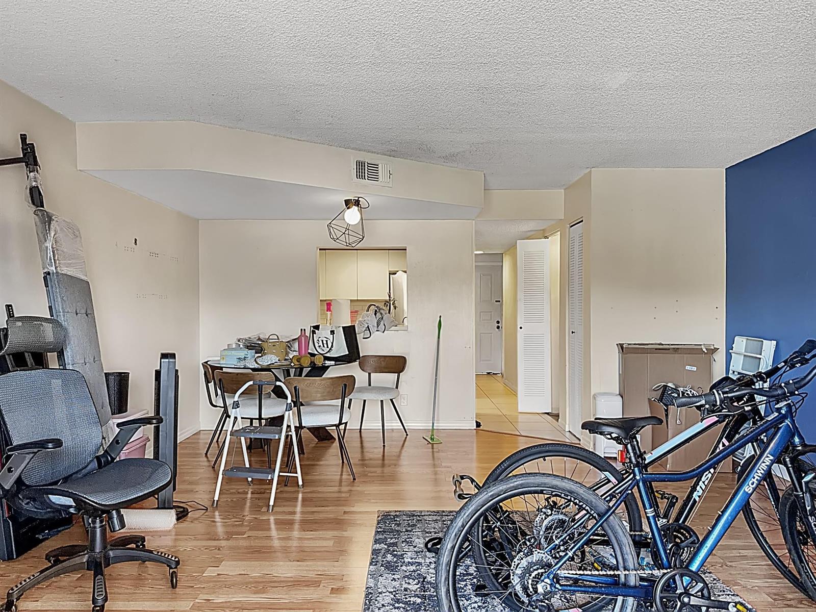 A living area with wood-look flooring, a dining set, and bicycles parked on a rug — 65 Deer Creek Road # H206, Deerfield Beach FL 33442, DEERFIELD BEACH, FL