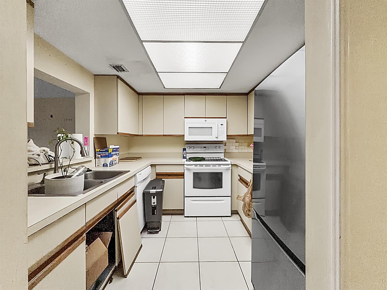 A kitchen features white appliances, light-colored cabinetry with wood trim, and white tile flooring — 65 Deer Creek Road # H206, Deerfield Beach FL 33442, DEERFIELD BEACH, FL
