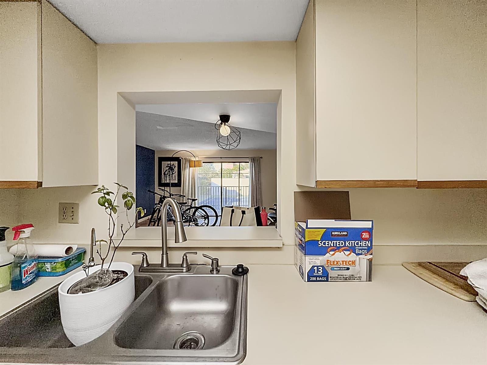 A kitchen sink area features a pass-through window looking into a living room — 65 Deer Creek Road # H206, Deerfield Beach FL 33442, DEERFIELD BEACH, FL