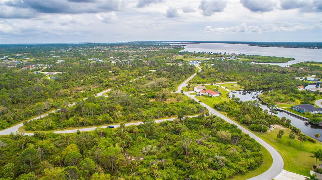 An aerial view shows a residential area with wooded lots, paved roads, and a canal — 1310 BRAKLET TERRACE, PORT CHARLOTTE, FL