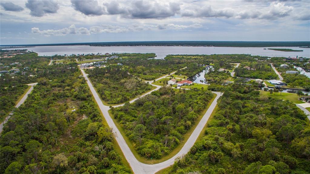 An aerial view shows a vacant, wooded residential lot bordered by paved roads near water — 1310 BRAKLET TERRACE, PORT CHARLOTTE, FL