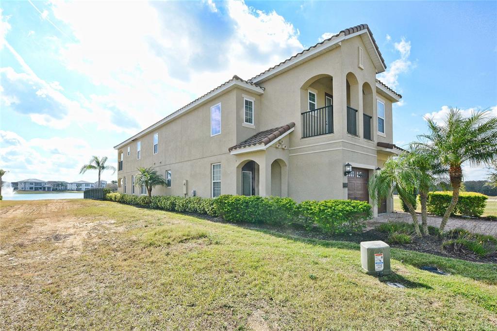 A two-story stucco house with a balcony and a garage sits beside a lake — 7824 LOXAHATCHEE COURT, REUNION, FL