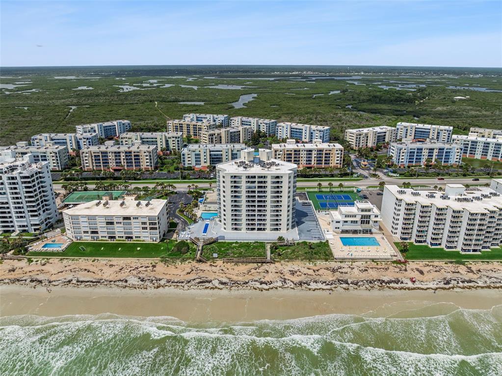 An aerial view shows multiple beachfront condominium buildings with swimming pools and tennis courts — 5207 S ATLANTIC AVENUE UNIT 425, NEW SMYRNA BEACH, FL