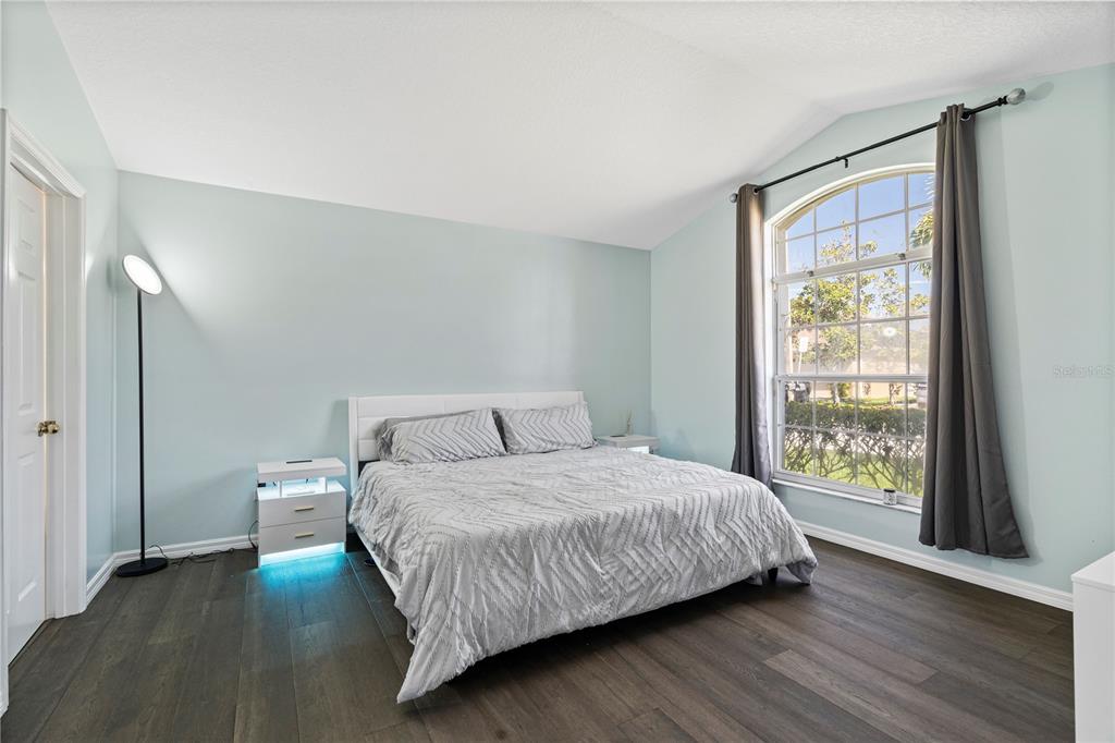 A bedroom with light blue walls, dark wood flooring, a bed, and an arched window — 215 ELDERBERRY DRIVE, DAVENPORT, FL