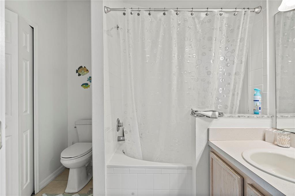 A bathroom features a white tiled shower-tub combination, a toilet, and a vanity with a mirror — 215 ELDERBERRY DRIVE, DAVENPORT, FL