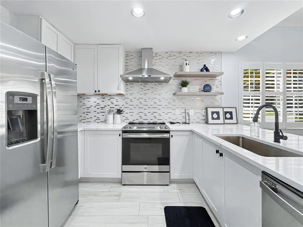 A modern kitchen features white cabinets, stainless steel appliances, a tiled backsplash, and quartz countertops — 3701 54TH DRIVE W UNIT 104, BRADENTON, FL