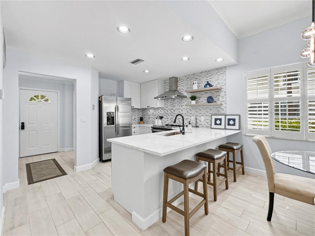 A modern kitchen features white cabinetry, a marble-topped island with bar stools, and stainless appliances — 3701 54TH DRIVE W UNIT 104, BRADENTON, FL