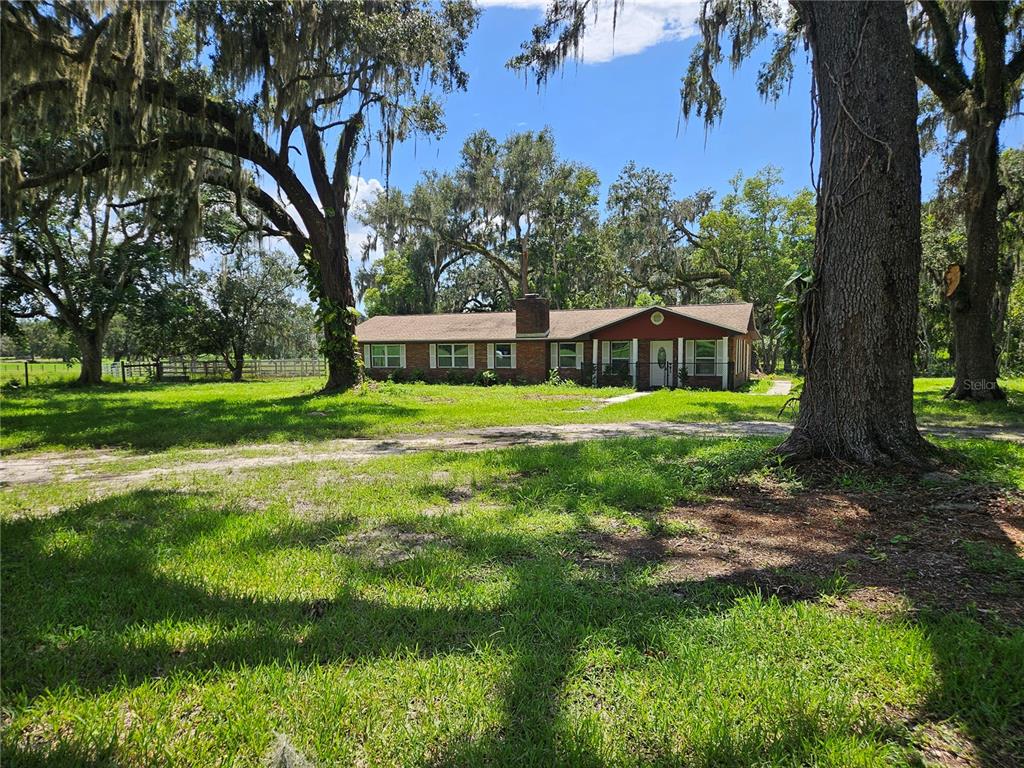 A single-story brick house with a red exterior sits on a grassy lot with trees — 16225 BELLAMY BROTHERS BOULEVARD, DADE CITY, FL