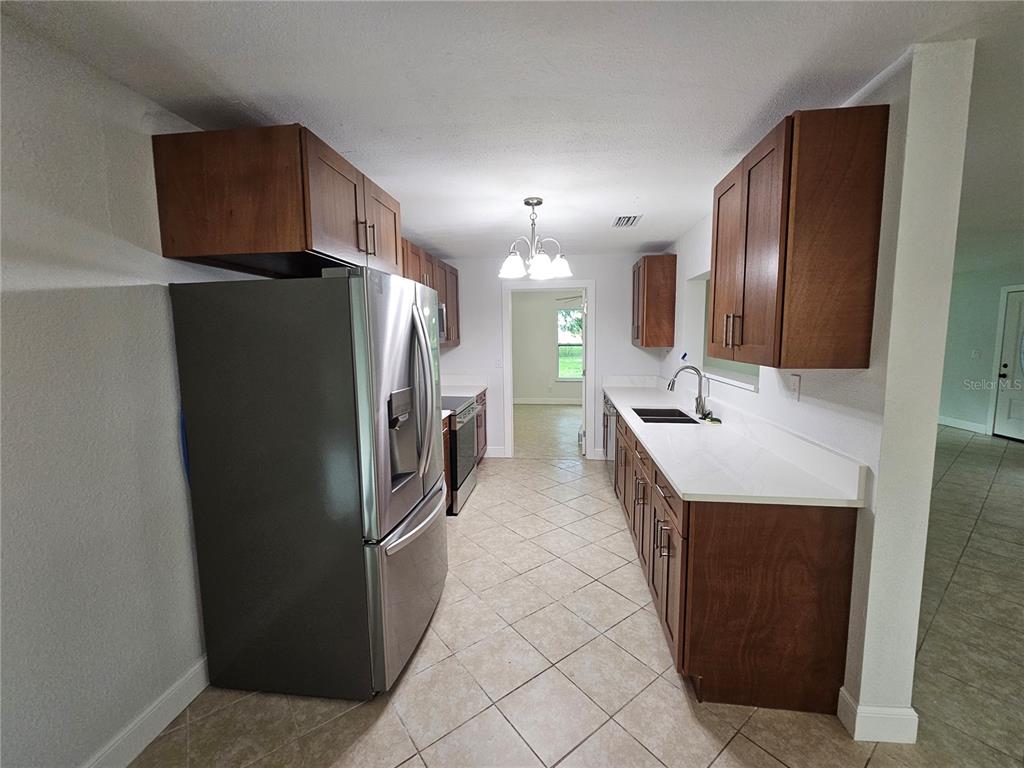 A kitchen features wood cabinets, stainless steel appliances, white countertops, and tile flooring — 16225 BELLAMY BROTHERS BOULEVARD, DADE CITY, FL